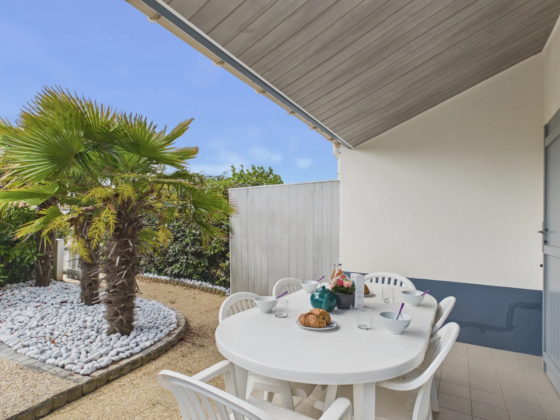 A covered outdoor dining area with a white table beside a palm tree.