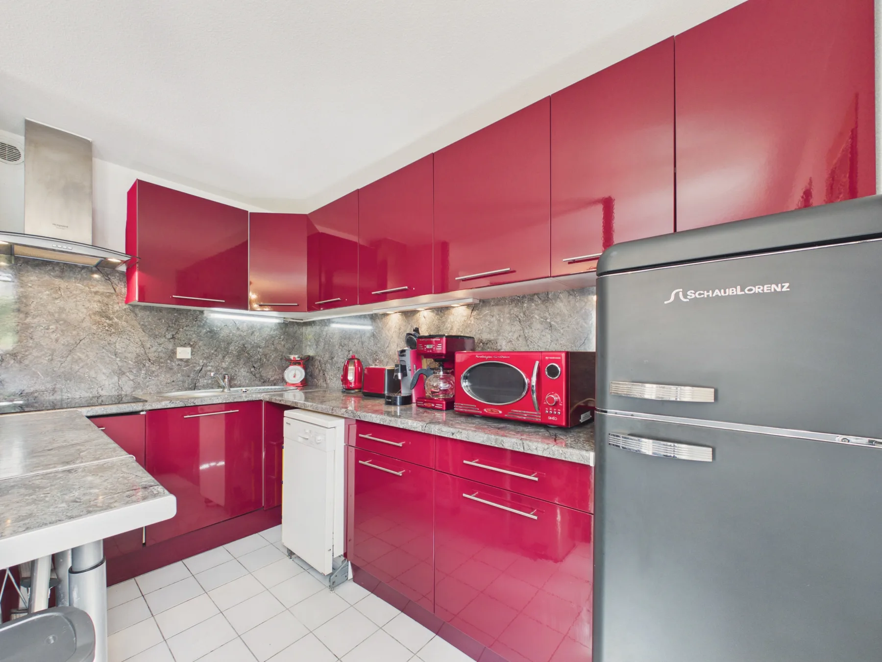 A kitchen with red cabinets, gray countertops, and small appliances.