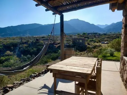 Una mesa de madera y una hamaca al aire libre dan a un paisaje montañoso.
