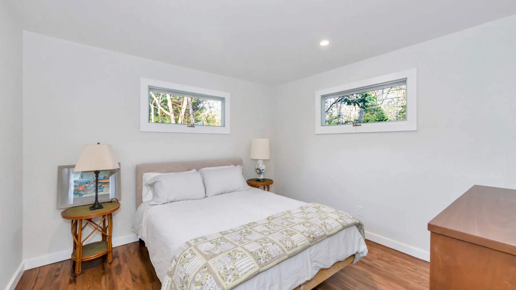 Un dormitorio con una cama bajo dos ventanas altas y suelo de madera.