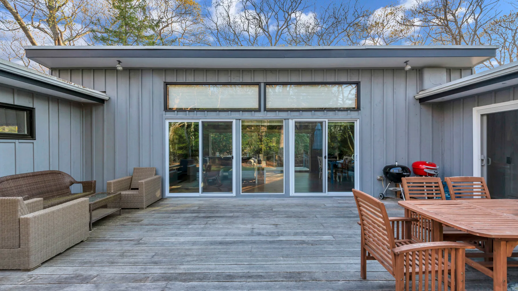 Una terraza exterior con mesa y asientos junto a una casa gris.