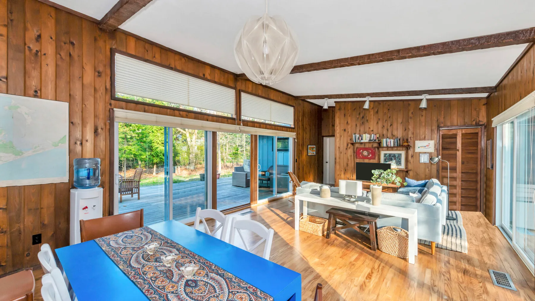 A wood-paneled living and dining area opens onto a garden through large glass doors.