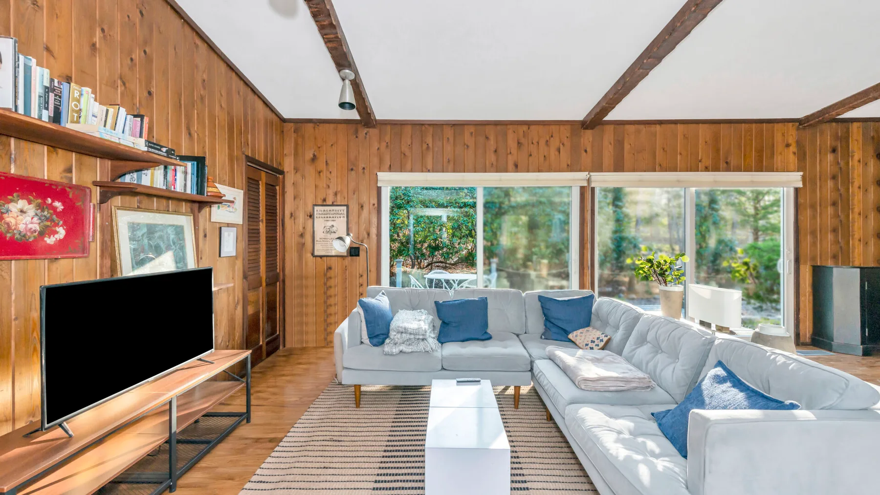 Una sala con paredes de madera, asientos, un televisor y ventanales.