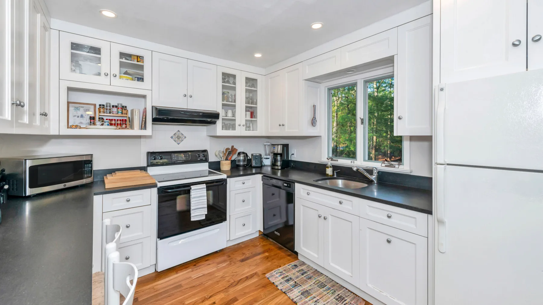 Una cocina luminosa con gabinetes blancos, encimeras oscuras y una ventana.