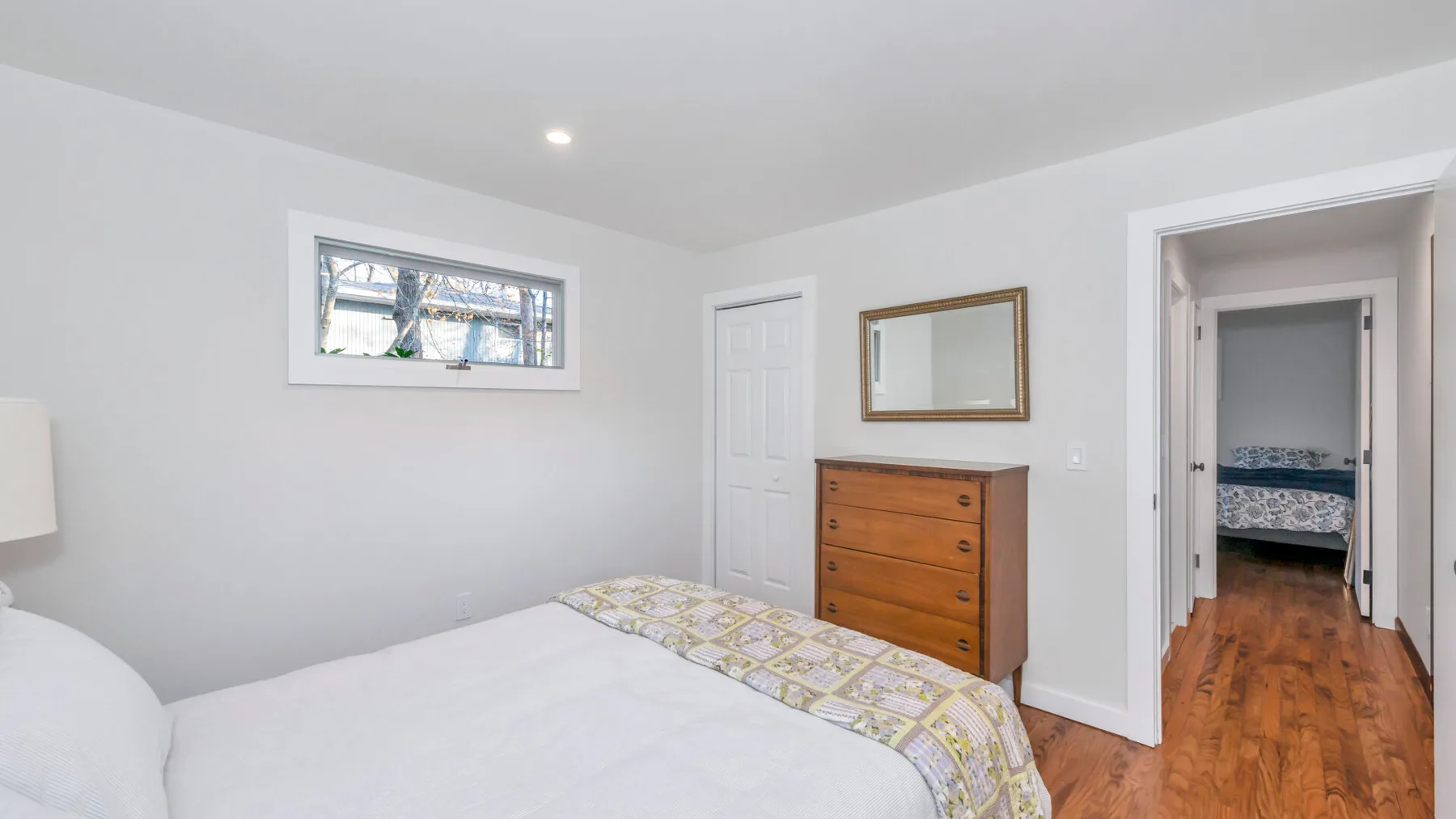 Un dormitorio con una cama, una cómoda de madera y una puerta hacia un pasillo.
