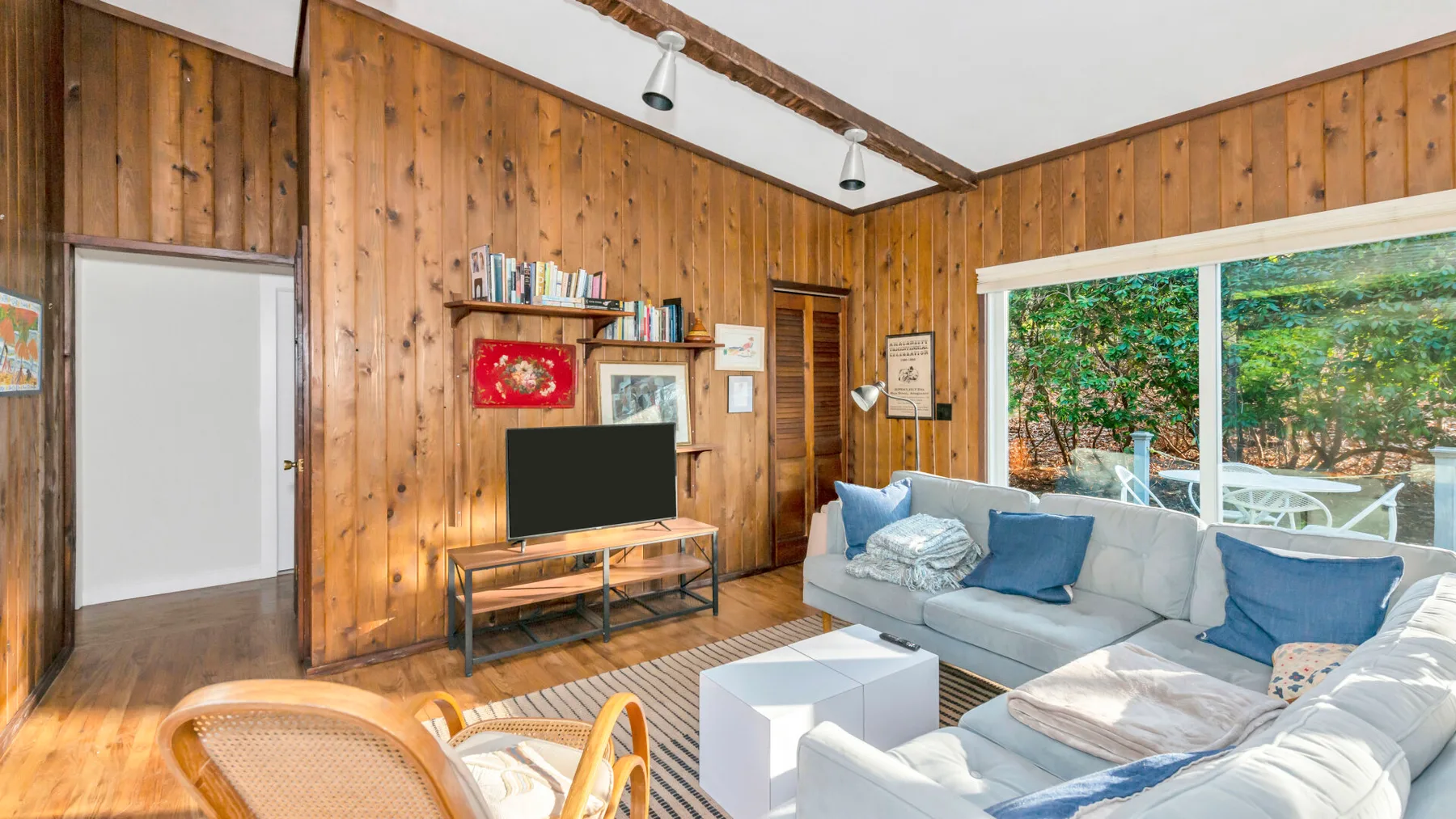 Una sala de estar revestida de madera, con asientos y grandes ventanas frente a la vegetación.