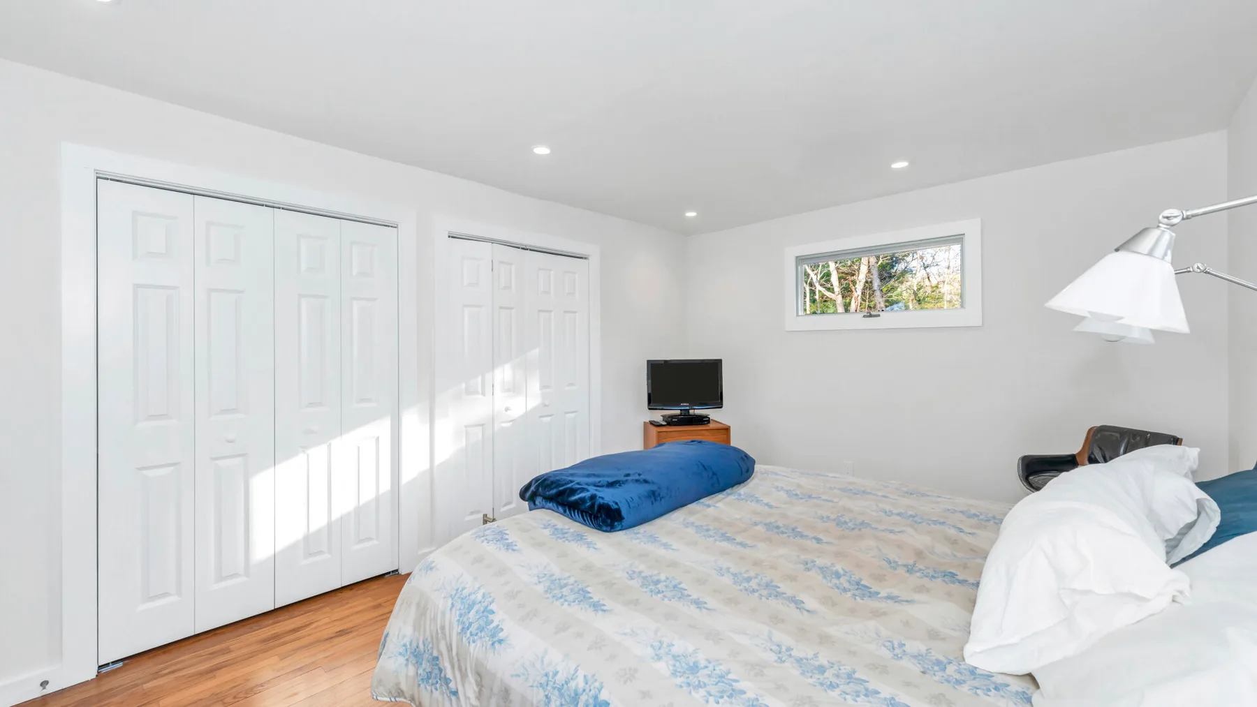 Un dormitorio luminoso con una cama, puertas blancas con paneles y una ventana pequeña.