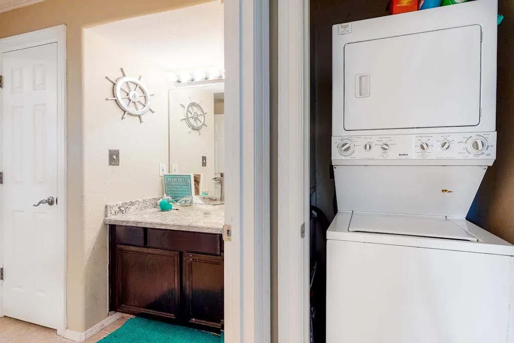 Un lavabo de baño con espejo y decoración náutica está junto a una lavadora y secadora apiladas.