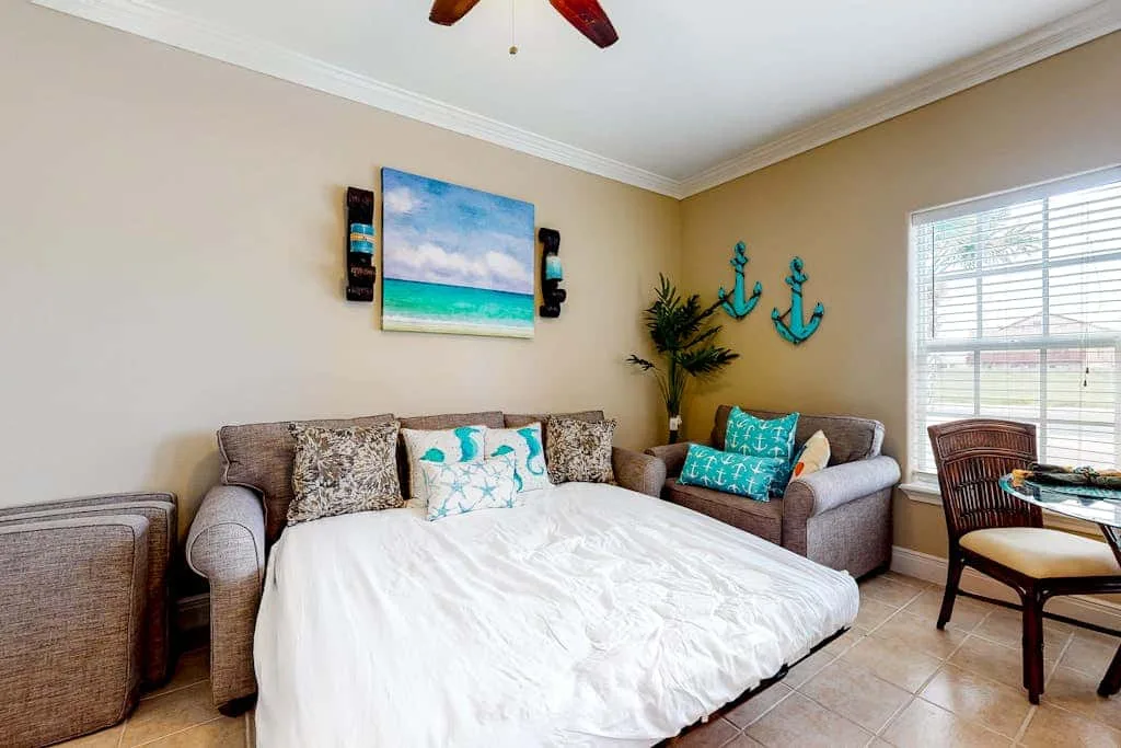 Una sala de estar con sofá cama, cojines coloridos y arte de temática costera.