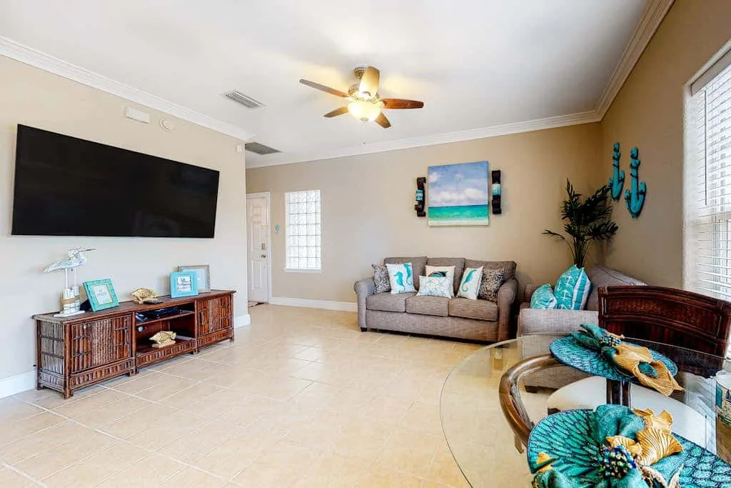 A living room with seating, a wall-mounted television, and a glass coffee table.