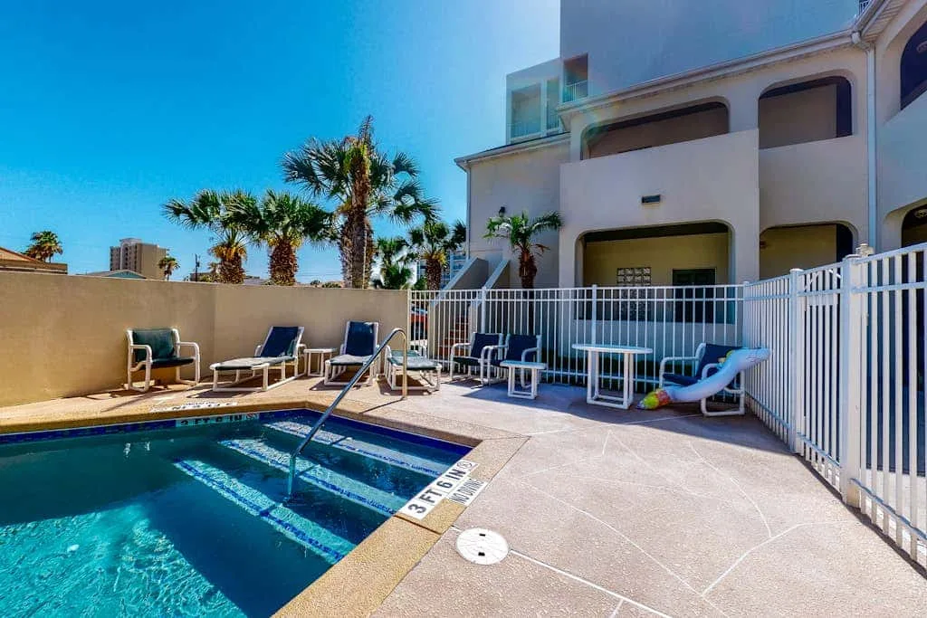 Una piscina al aire libre está junto a un patio pavimentado con asientos.