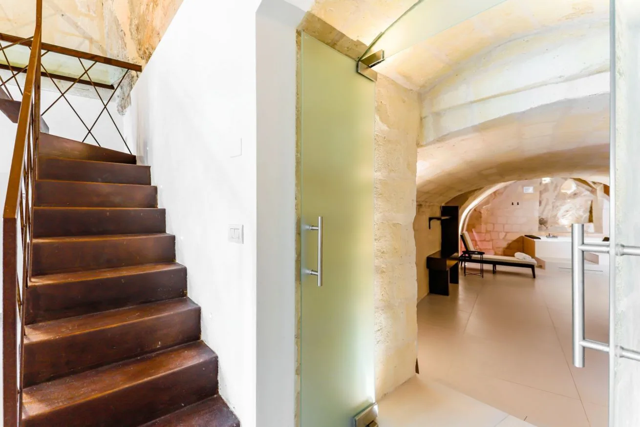 A staircase and open glass door lead into a bright room with an arched stone ceiling.