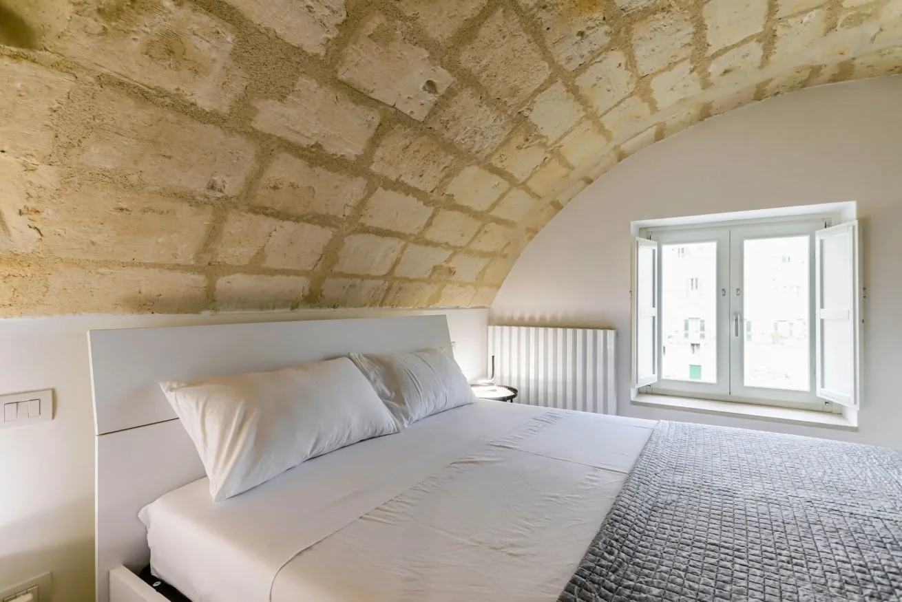 A bedroom with a bed beneath a curved stone ceiling and a window.