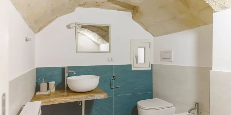 A bathroom with a white vessel sink and teal tiled walls.