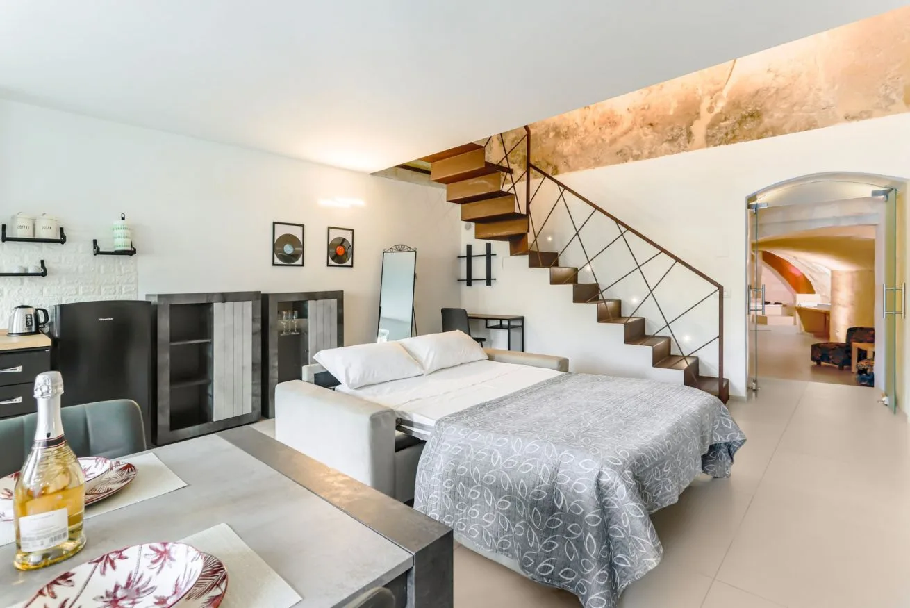 A bedroom with a bed beneath a staircase and dark storage cabinets.