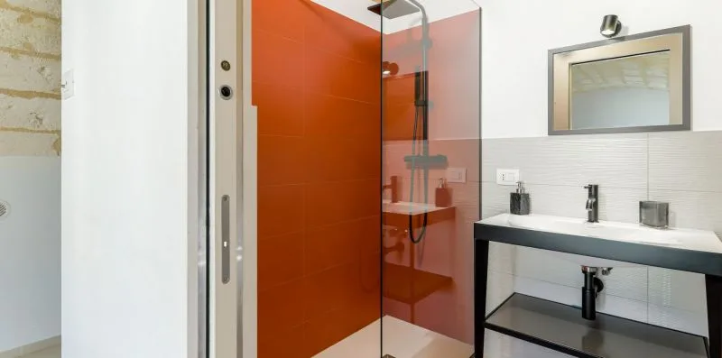 A modern bathroom with an orange shower wall and a dark vanity.