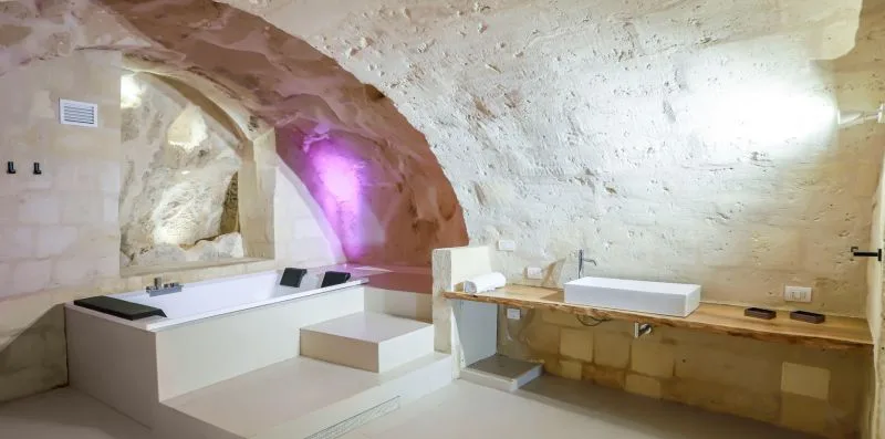 A bathroom with a bathtub, sink, and rough stone walls.