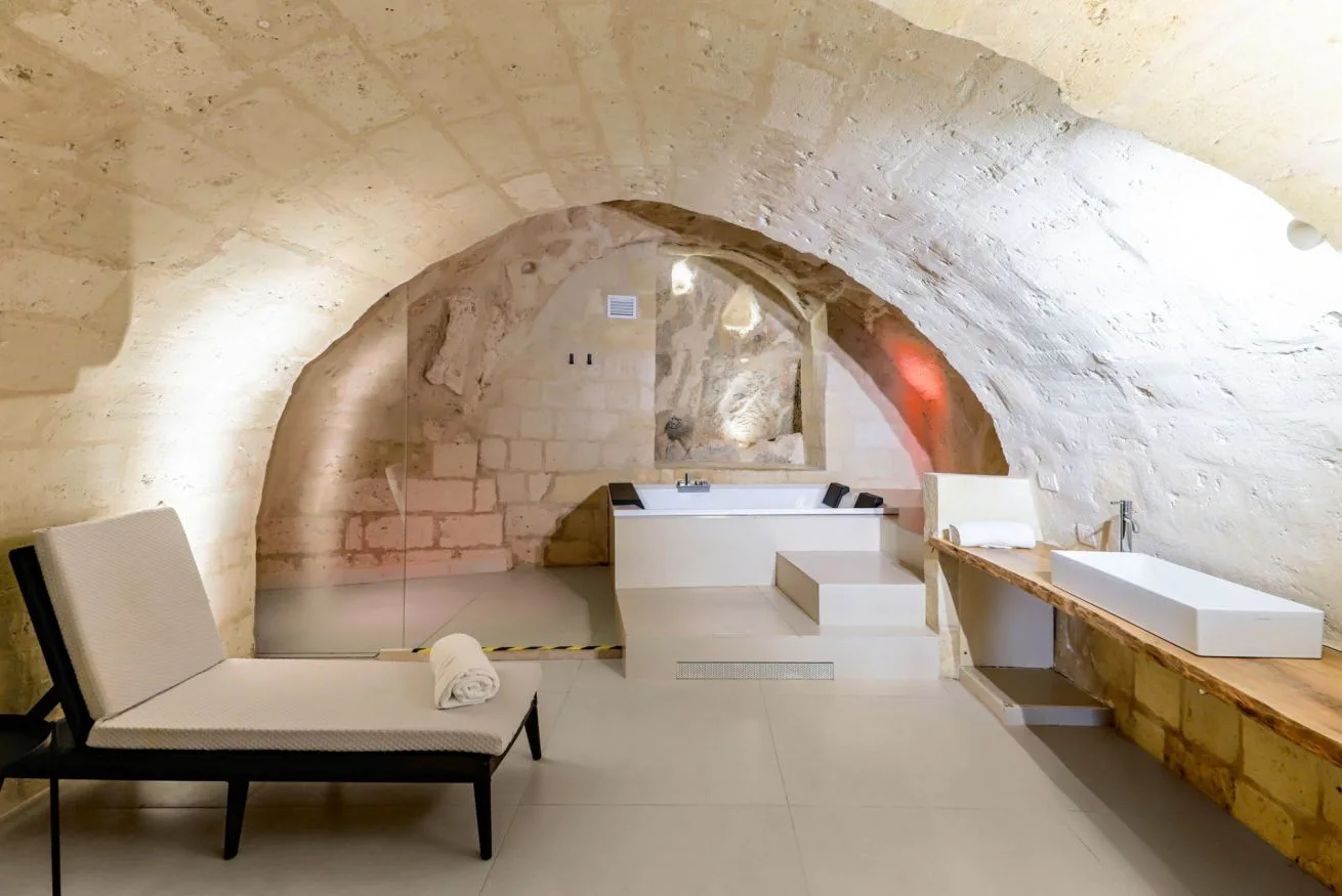 A spa bathing area beneath a stone arch, with a built-in tub and lounge seating.