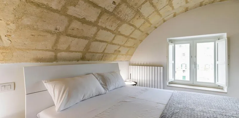 A bedroom with a bed beneath a curved stone ceiling and a window.