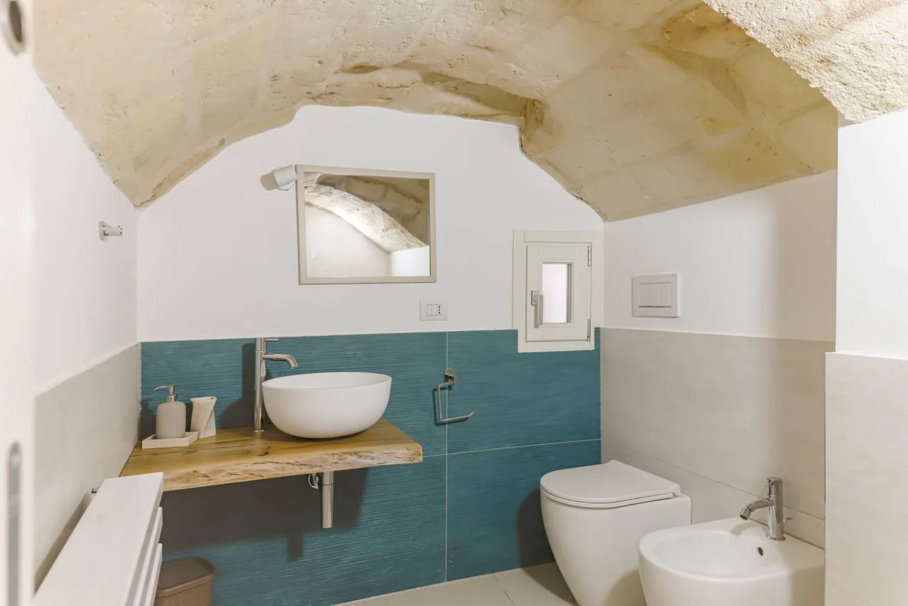 A bathroom with a vessel sink, toilet, and teal tiled walls.