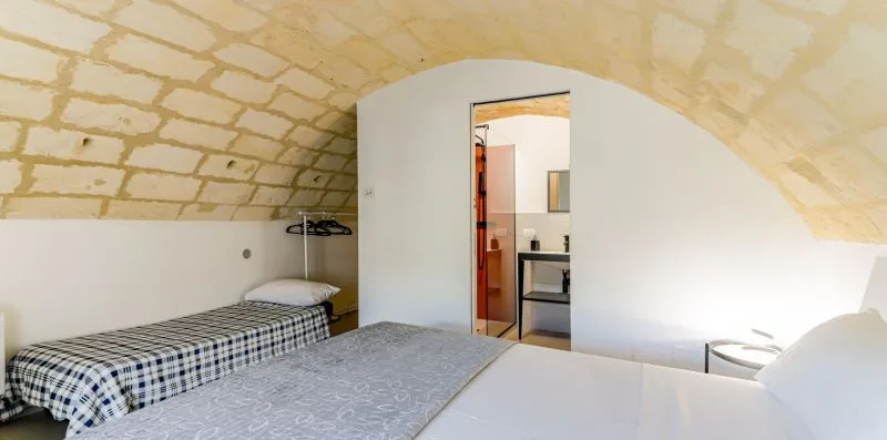 A bedroom beneath a curved stone ceiling, with beds and an open doorway.