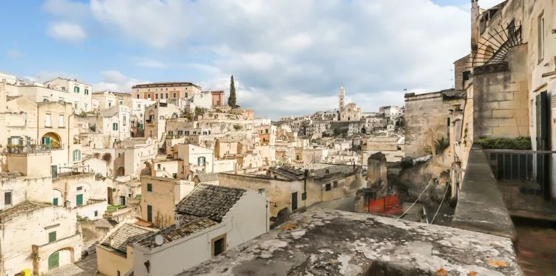 A hillside townscape of closely packed stone buildings beneath a cloudy sky.