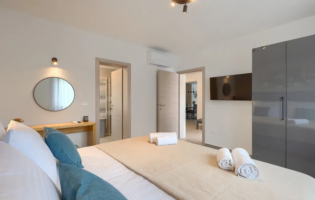 Un dormitorio luminoso con una cama bien tendida y un televisor en la pared.