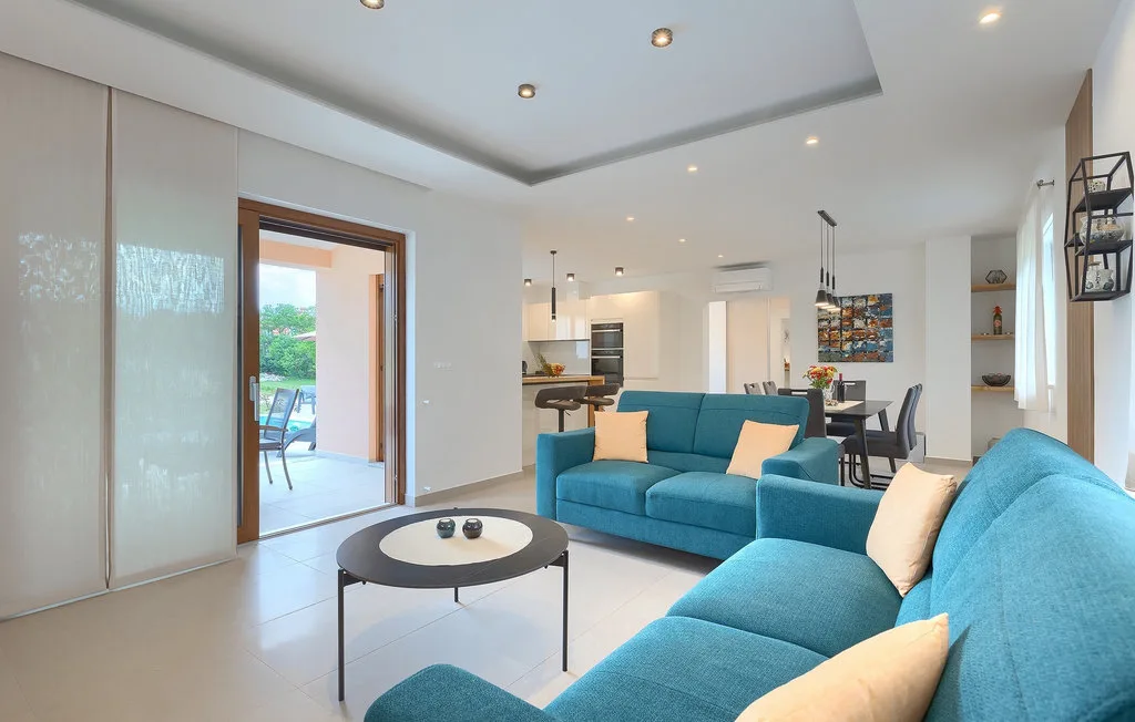 Una sala luminosa con asientos azules y una cocina y comedor abiertos.