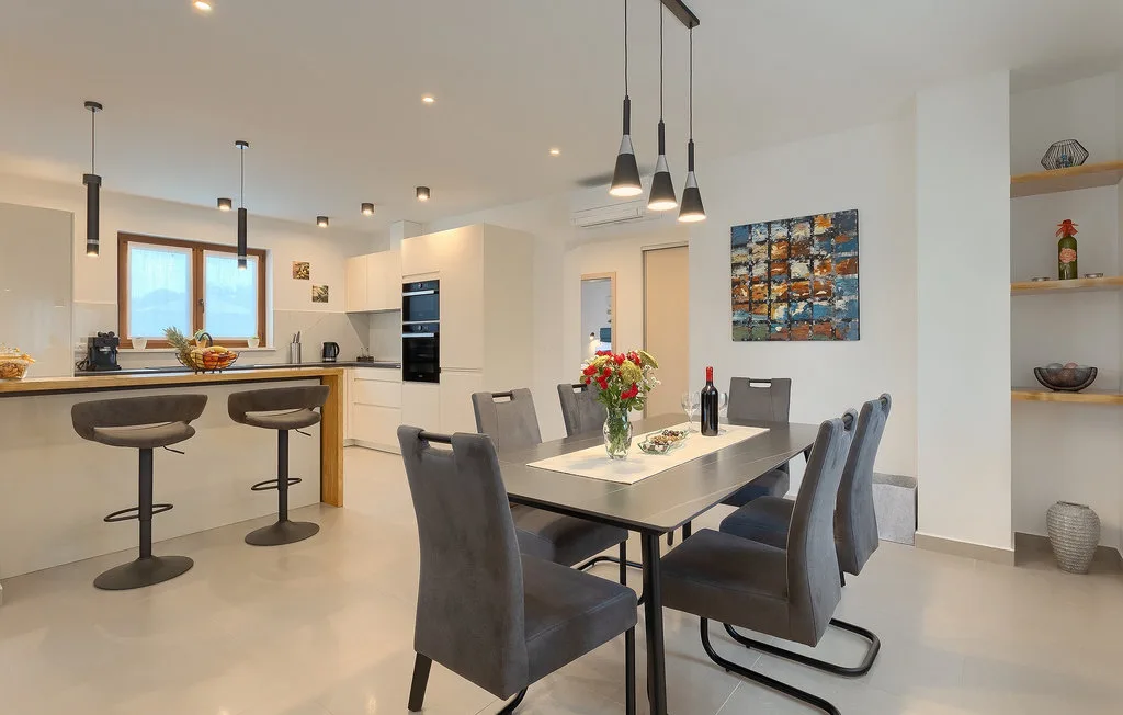 Comedor junto a una cocina abierta, con una mesa y lámparas colgantes.