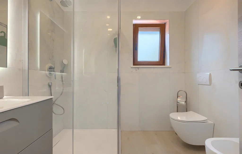 Un baño luminoso con ducha de vidrio, lavabo e inodoro.