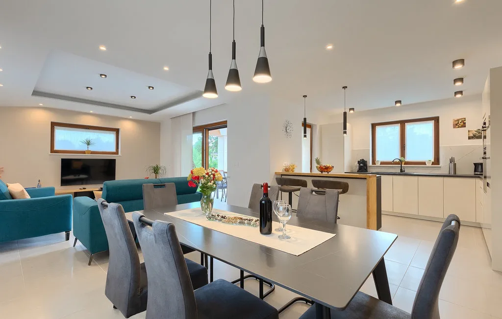 Comedor y cocina de planta abierta con una mesa, lámparas colgantes y una zona de estar contigua.