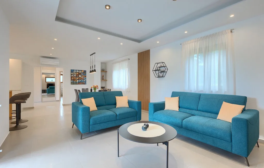 Una sala luminosa con asientos azules, una mesa de centro redonda y grandes ventanas con cortinas.