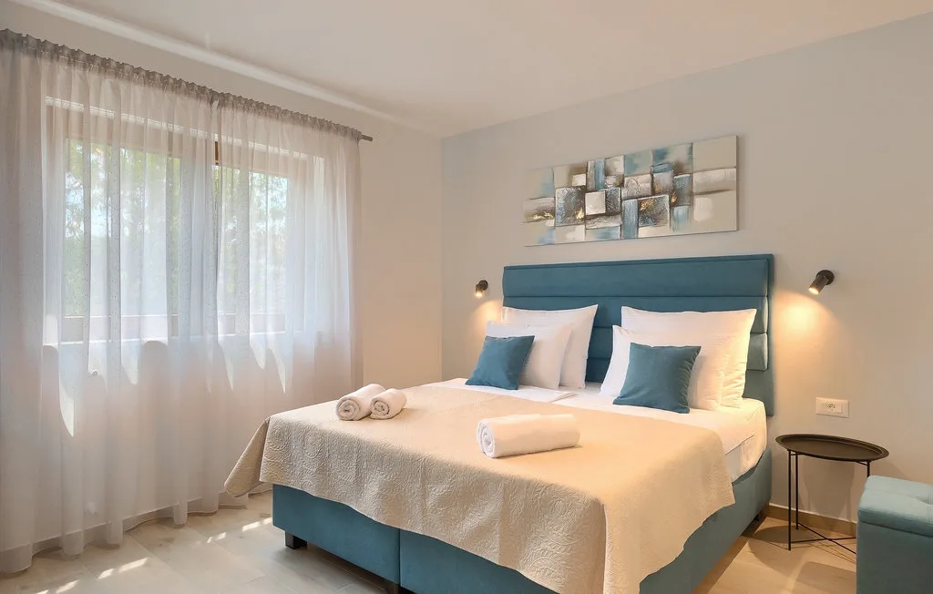 Un dormitorio con una cama bien arreglada y cortinas translúcidas en una ventana amplia.