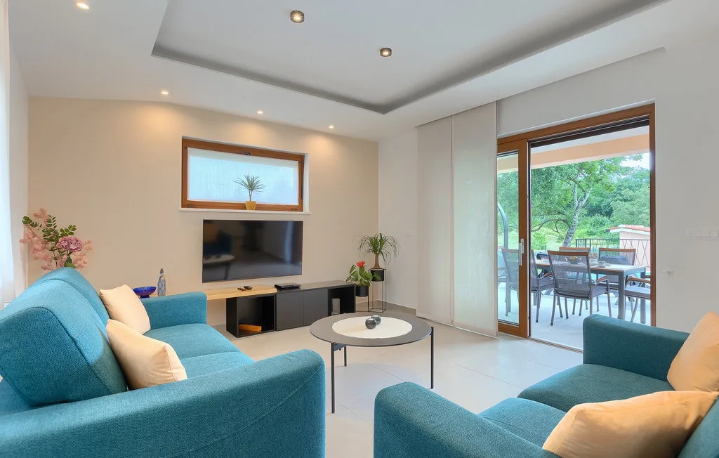 Una sala de estar con asientos color turquesa, un televisor y vista abierta a un patio.