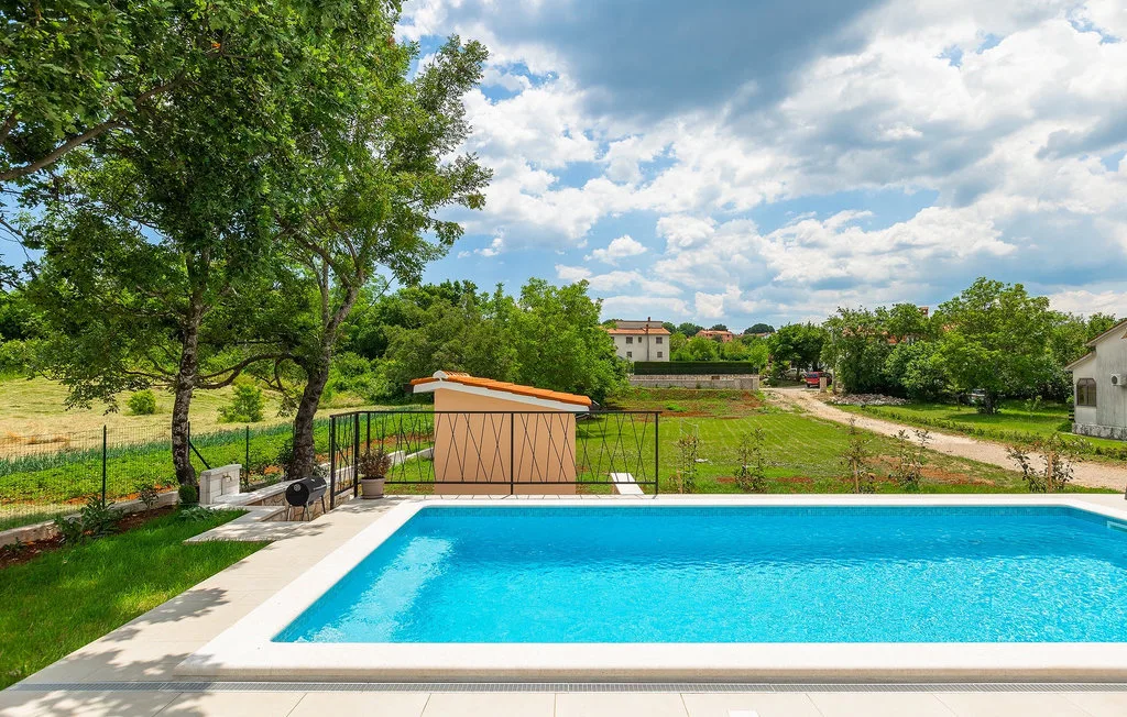 Una piscina al aire libre da a un paisaje verde bajo un cielo parcialmente nublado.