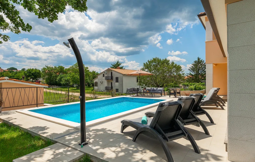Una piscina al aire libre está rodeada de asientos reclinables y un patio pavimentado.