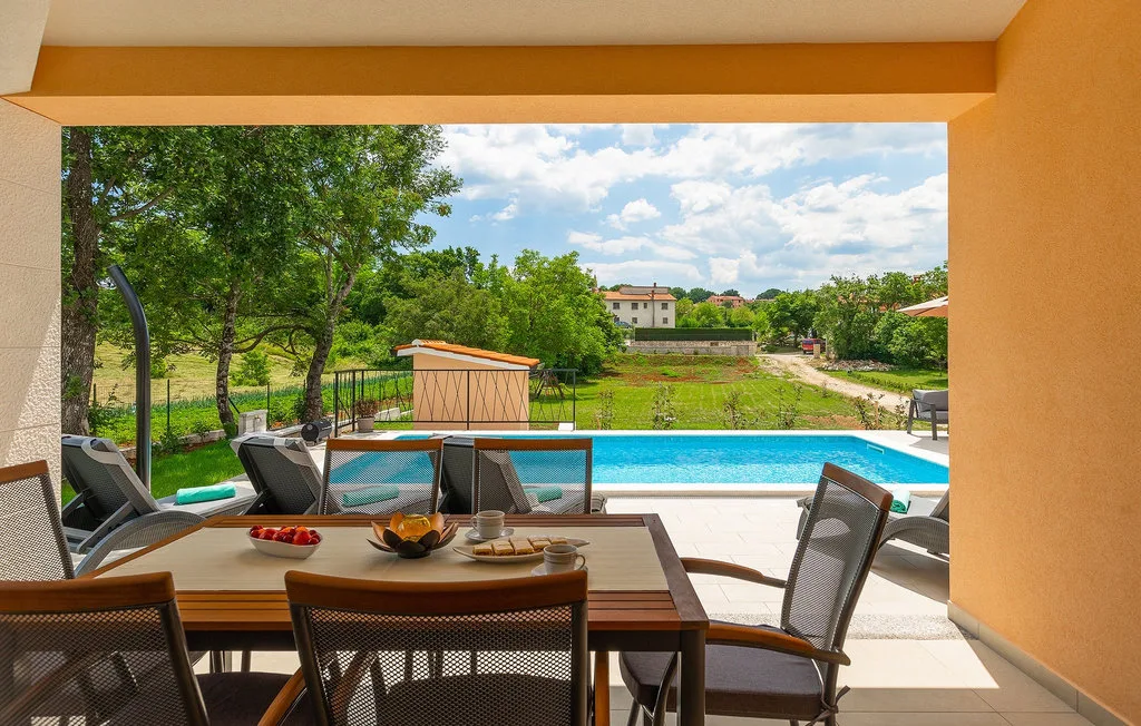 Comedor al aire libre con vistas a una piscina y un paisaje verde.