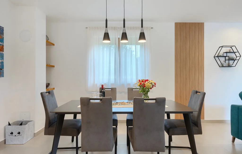 Comedor con una mesa rectangular, asientos grises y lámparas colgantes.