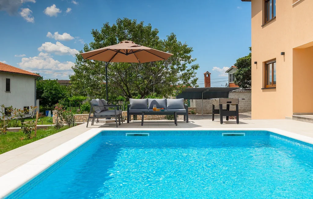 Una piscina al aire libre junto a una zona de estar en el patio con una sombrilla.
