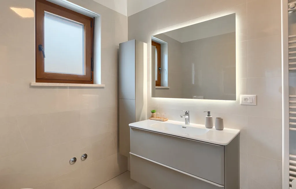 Un baño con lavabo, espejo grande y ventana.