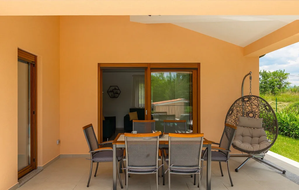 Un patio cubierto tiene una mesa de comedor y una silla colgante.