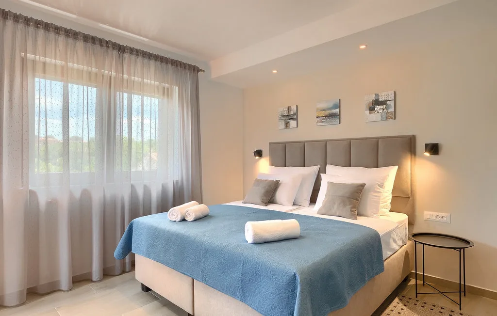 Un dormitorio con una cama bien tendida junto a una ventana con cortinas.