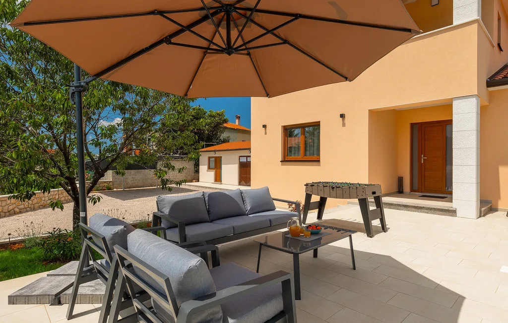 Un patio al aire libre tiene asientos acolchados y una mesa de futbolín bajo una gran sombrilla.
