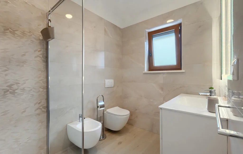 Un baño moderno con ducha de vidrio, inodoro suspendido y lavabo.