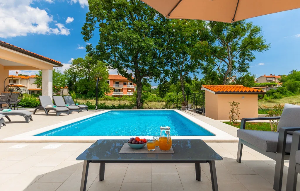 Una piscina al aire libre junto a un patio pavimentado con asientos y una mesa.