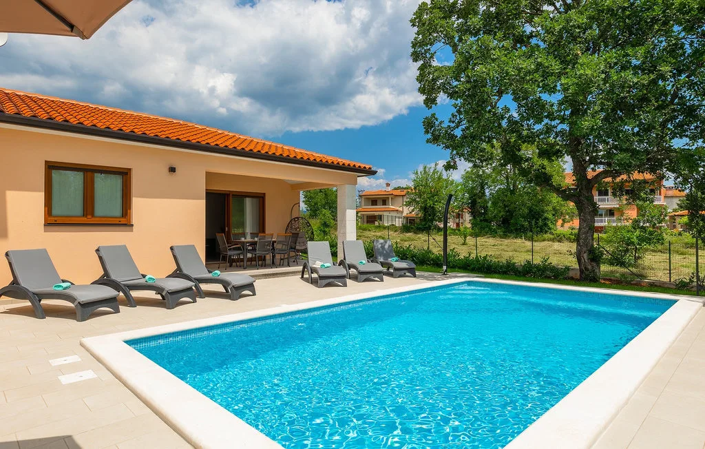 Una piscina al aire libre junto a una casa, con tumbonas en el patio.