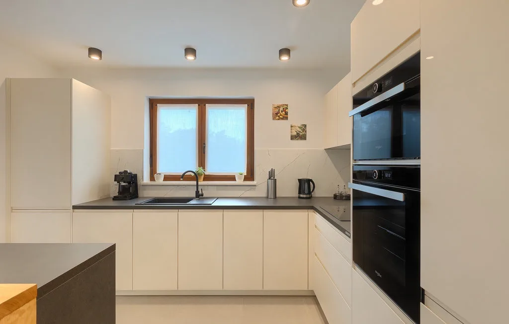 Una cocina moderna y luminosa con gabinetes claros, encimeras oscuras y una ventana sobre el fregadero.