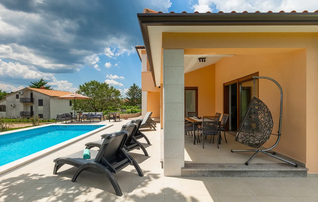 Un patio junto a una piscina tiene asientos para descansar y una zona de comedor cubierta.