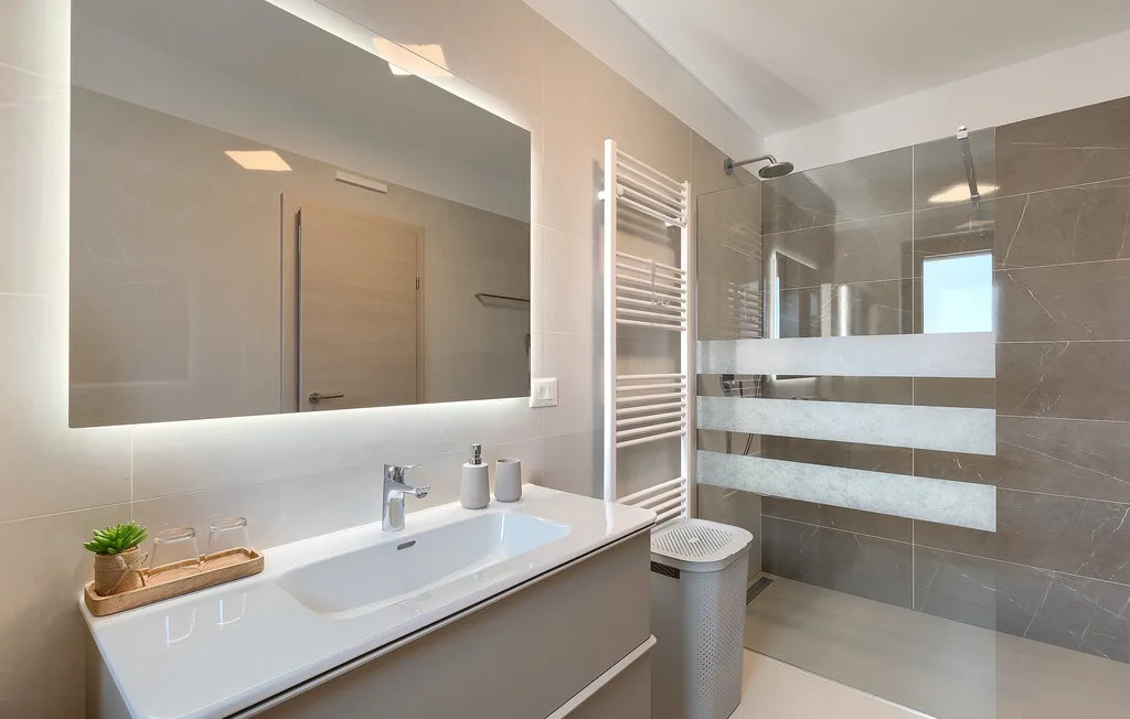 Un baño moderno con un lavabo largo, espejo de pared y ducha de vidrio.
