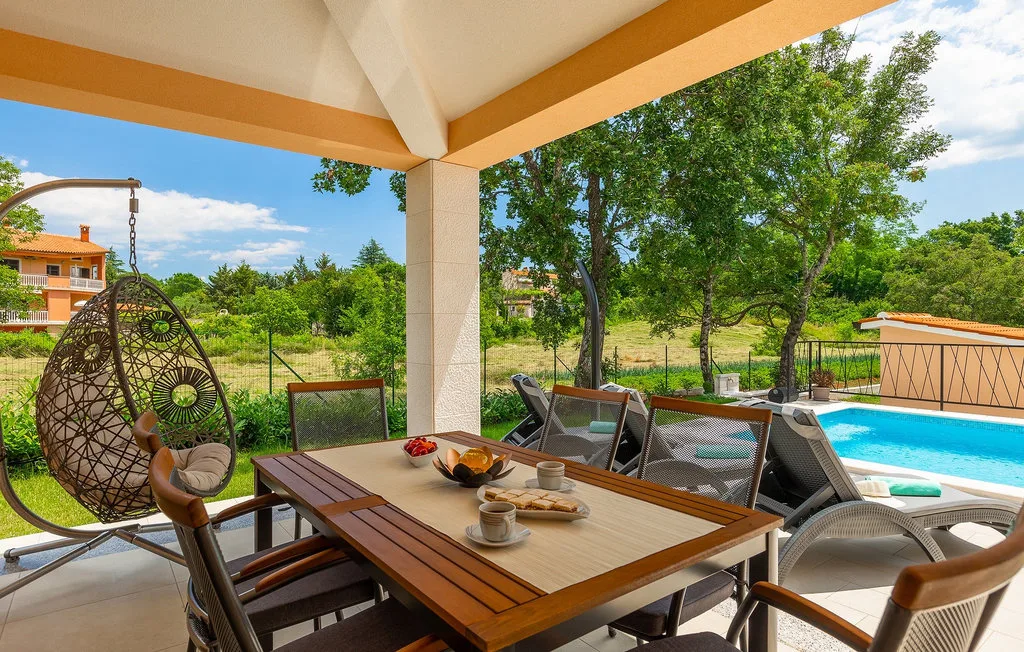 Una zona de comedor exterior cubierta da a un jardín y una piscina.
